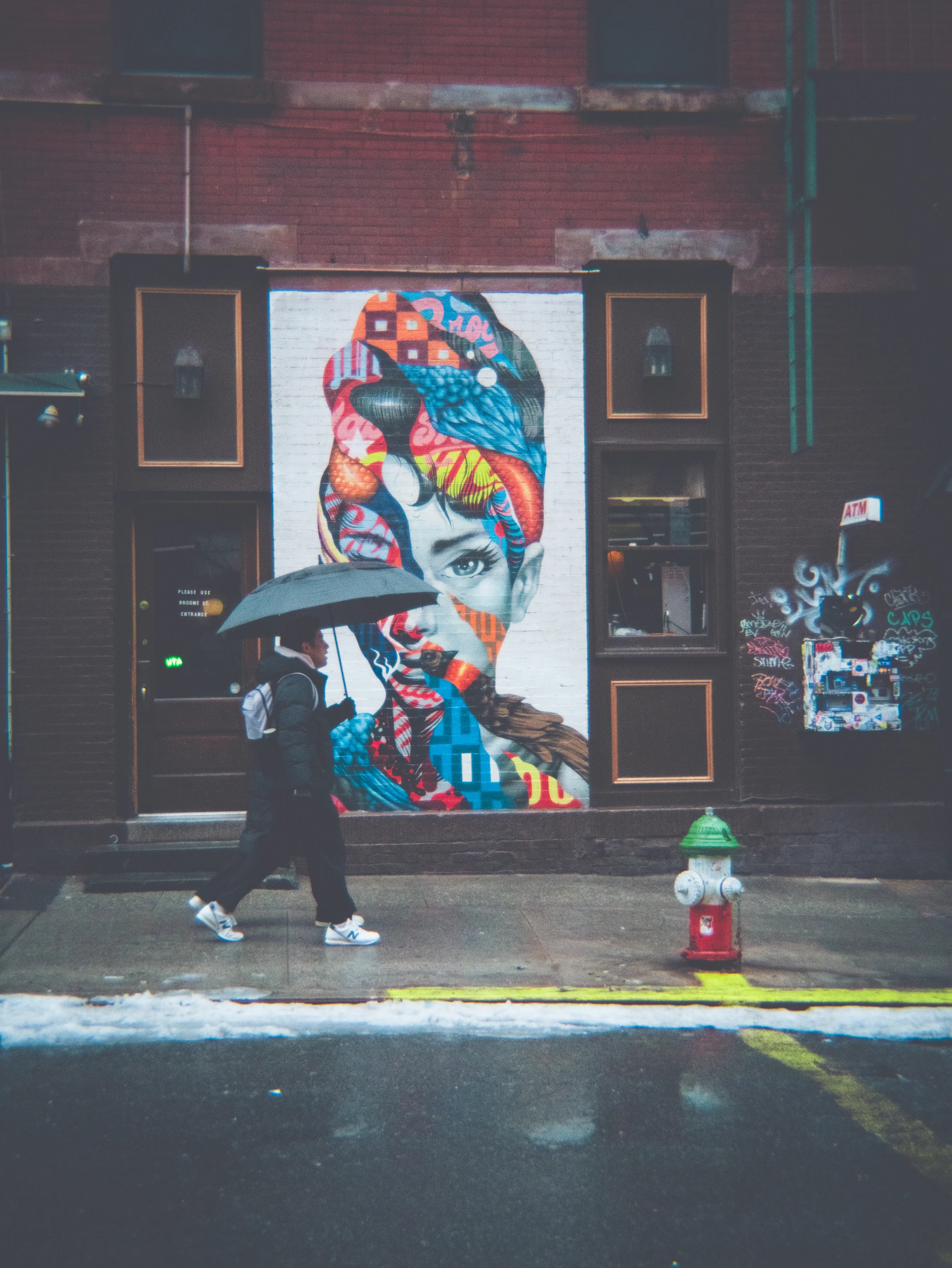 Passer-by with an umbrella in front of a colorful mural, New York
