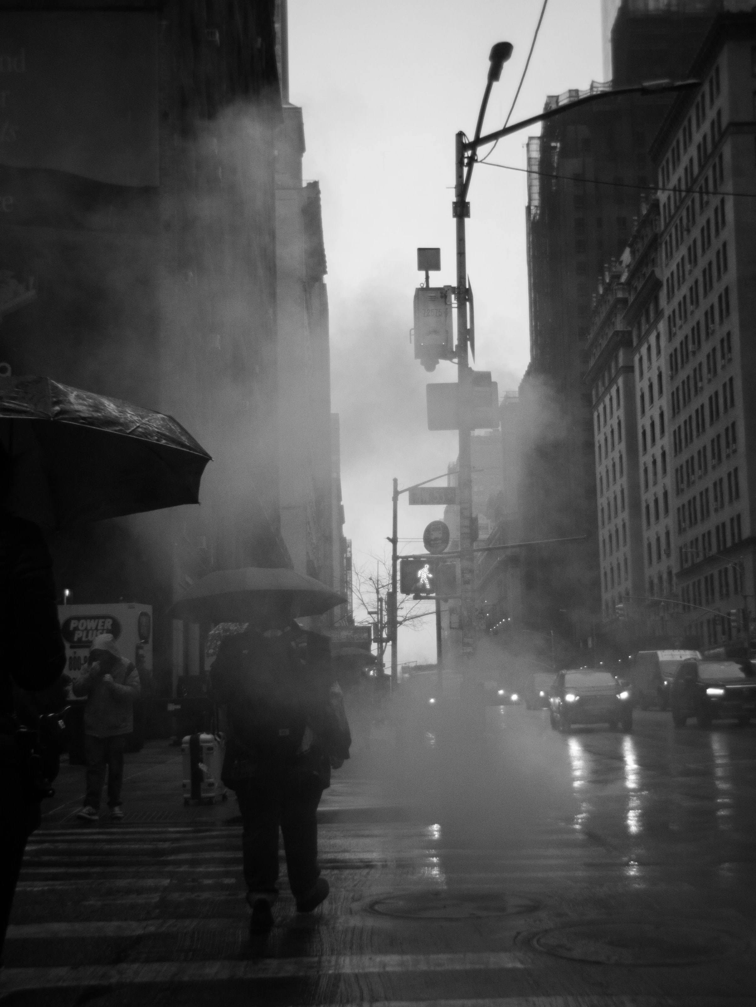 Pedestrians with umbrellas in the rain, steam over the street, New York