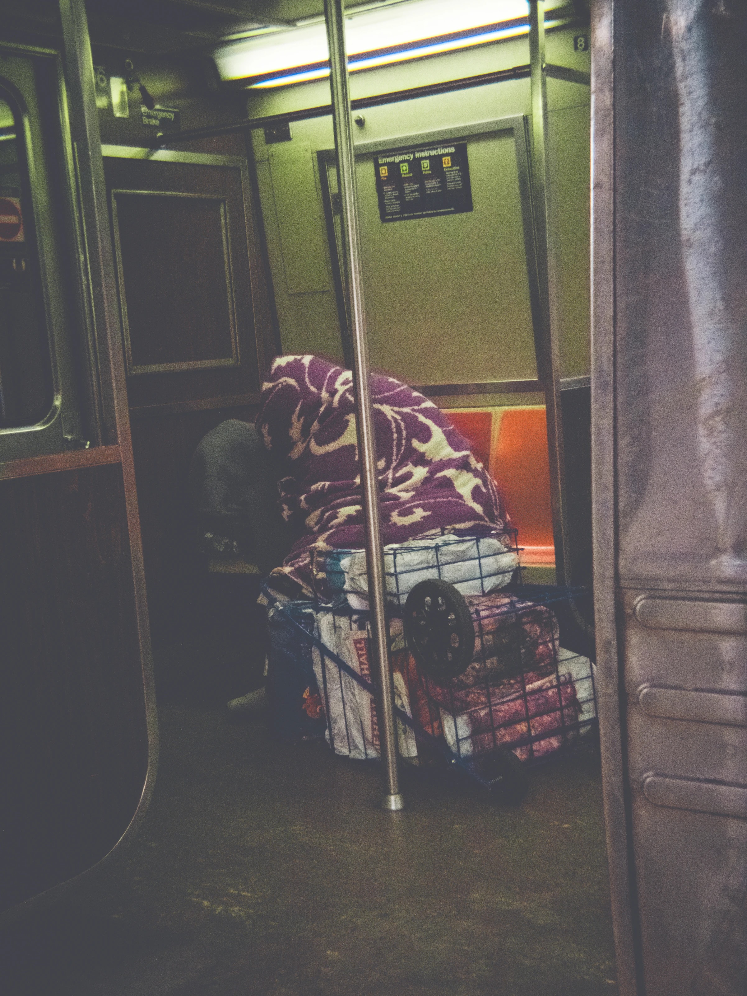 Person under a blanket beside a loaded luggage cart in the subway, New York