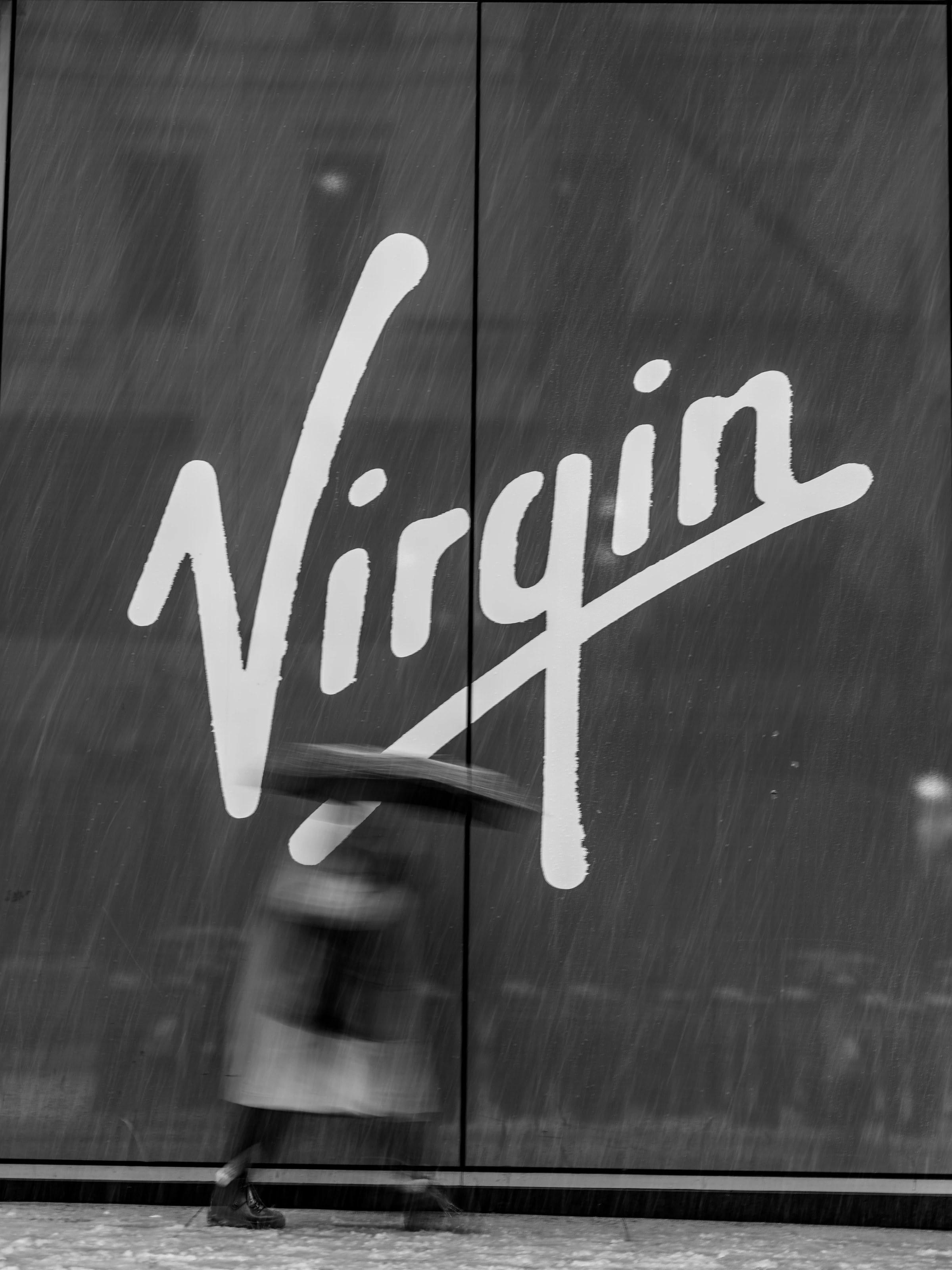 Virgin sign in driving snow, a person with an umbrella in front of it, New York